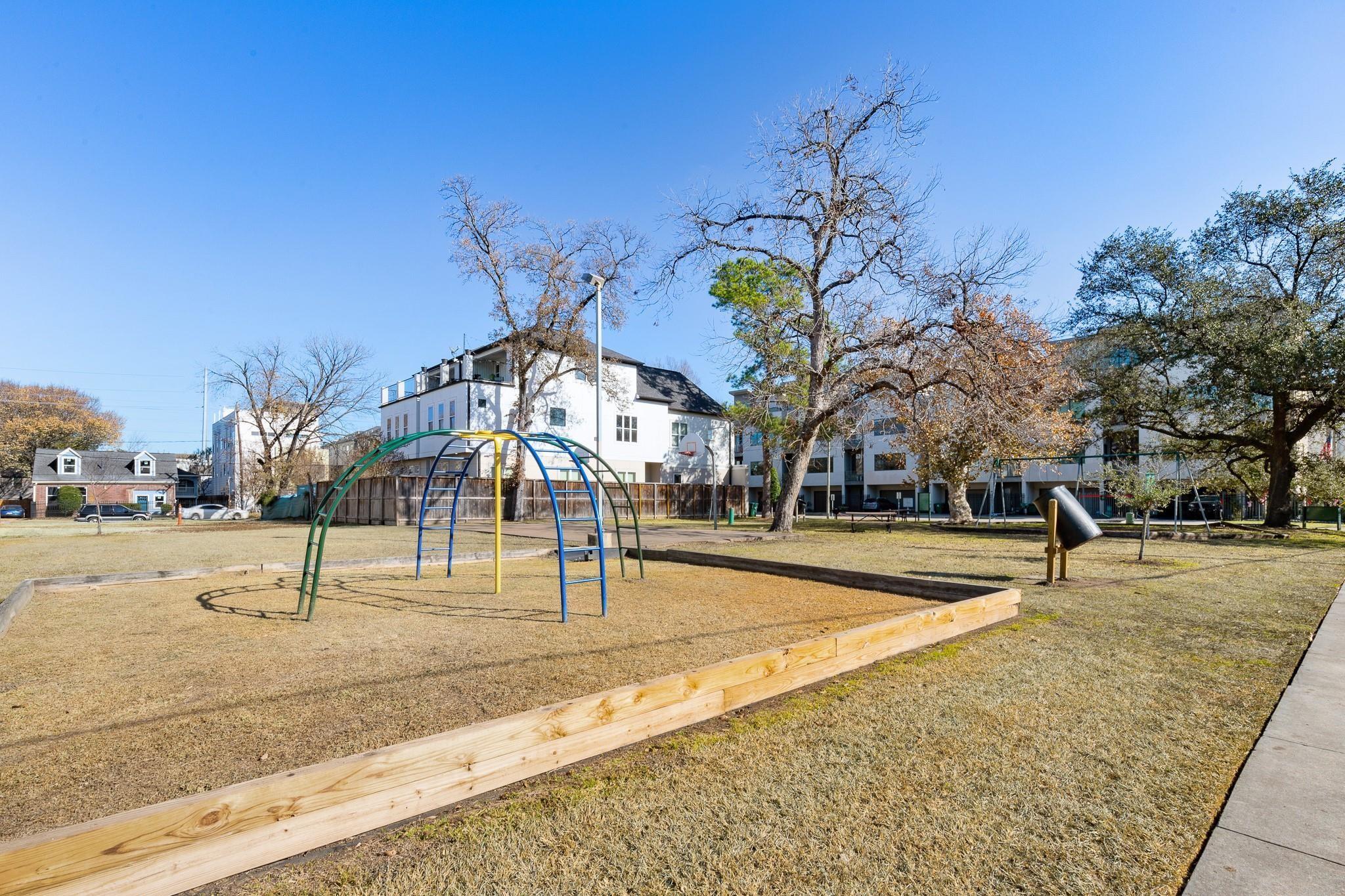 Neighborhood playground with colorful climbing bars, basketball hoop, and slide beside multi-story homes.