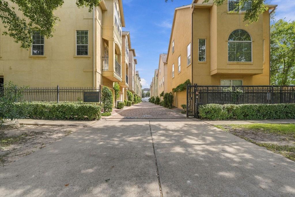 Gated entrance to a townhome community with beige homes along a brick-paved drive.
