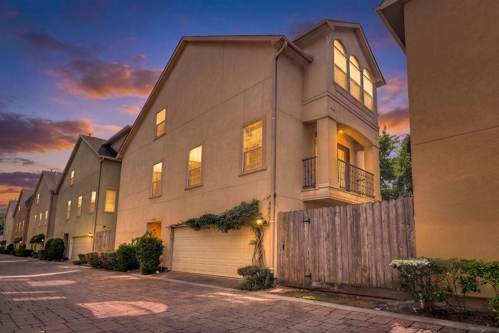 Attached townhome with a two-car garage and balcony glowing at dusk.