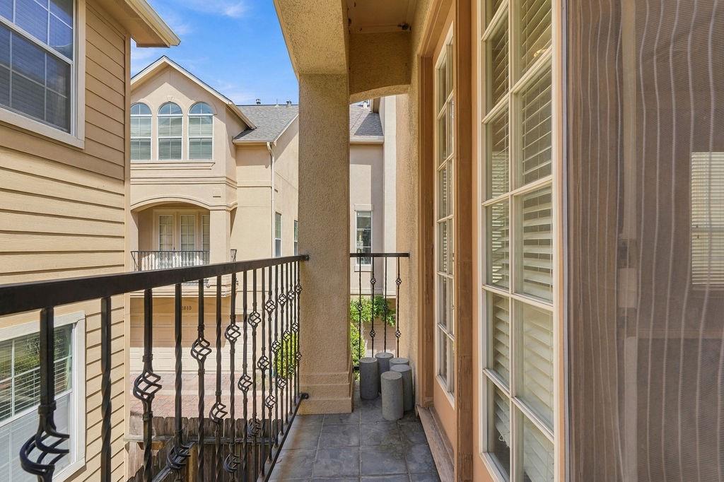 Narrow tiled balcony with black railings, tall windows, and views of neighboring townhouses.