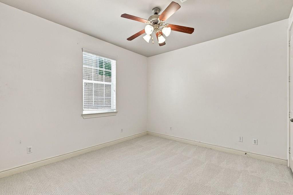 Empty bedroom with light carpet, window blinds, and a wood-blade ceiling fan.