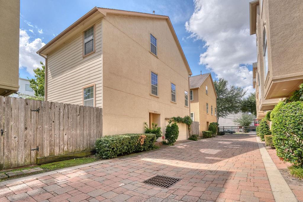 Beige multi-story townhouse beside a brick-paved driveway and wooden privacy fence.