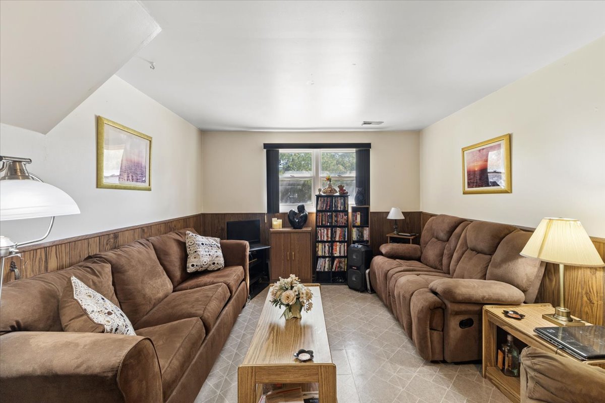 Living room with brown sofas and recliners, wood-paneled walls, and a central coffee table.