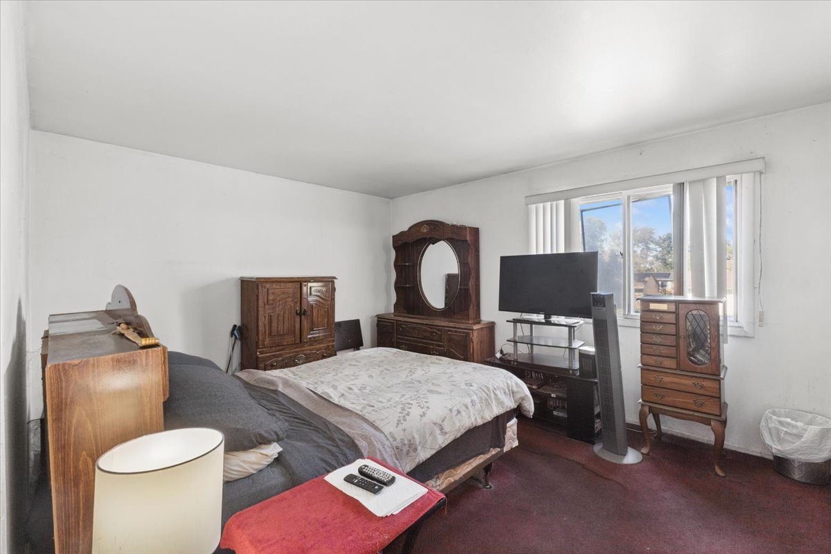 Bedroom with dark wooden dressers, a large mirror, and a window with vertical blinds.