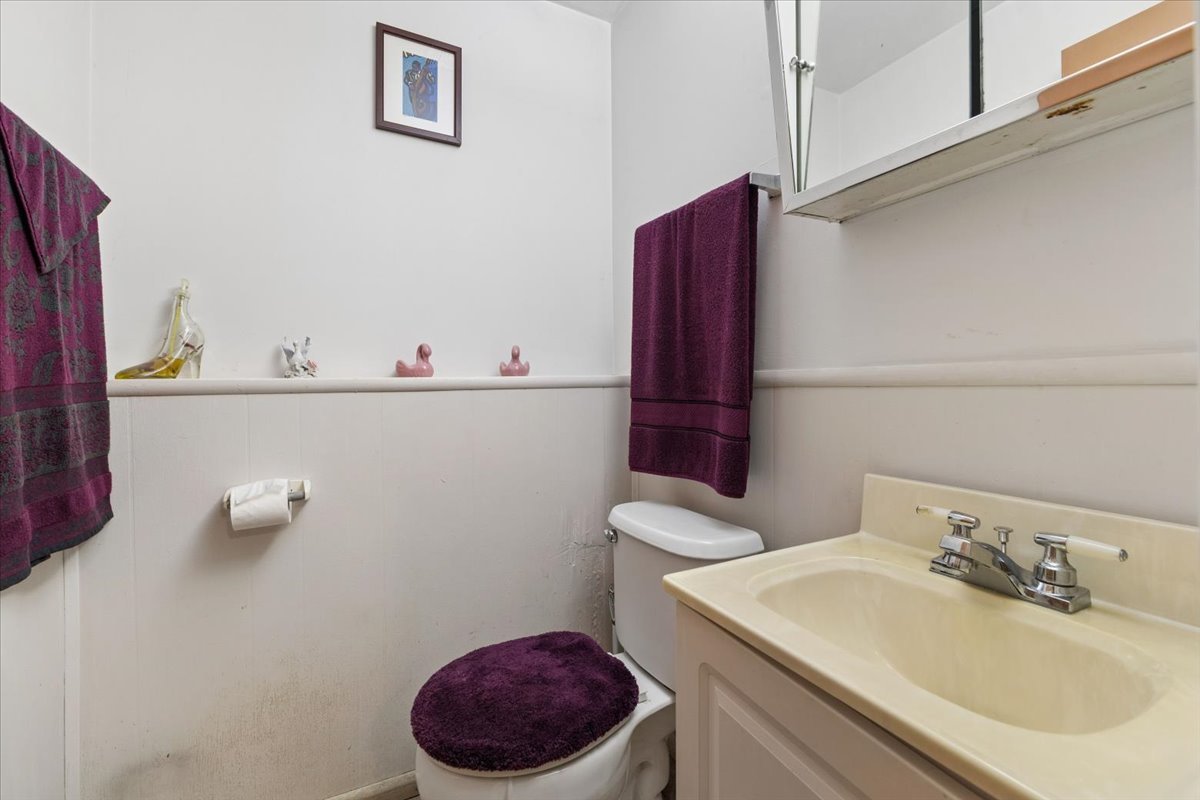 Bathroom with a cream vanity, toilet with purple seat cover, and matching purple towels.
