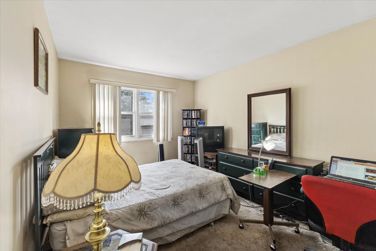 Furnished bedroom with a bed, dark green dresser and mirror, and a computer desk with a red chair.