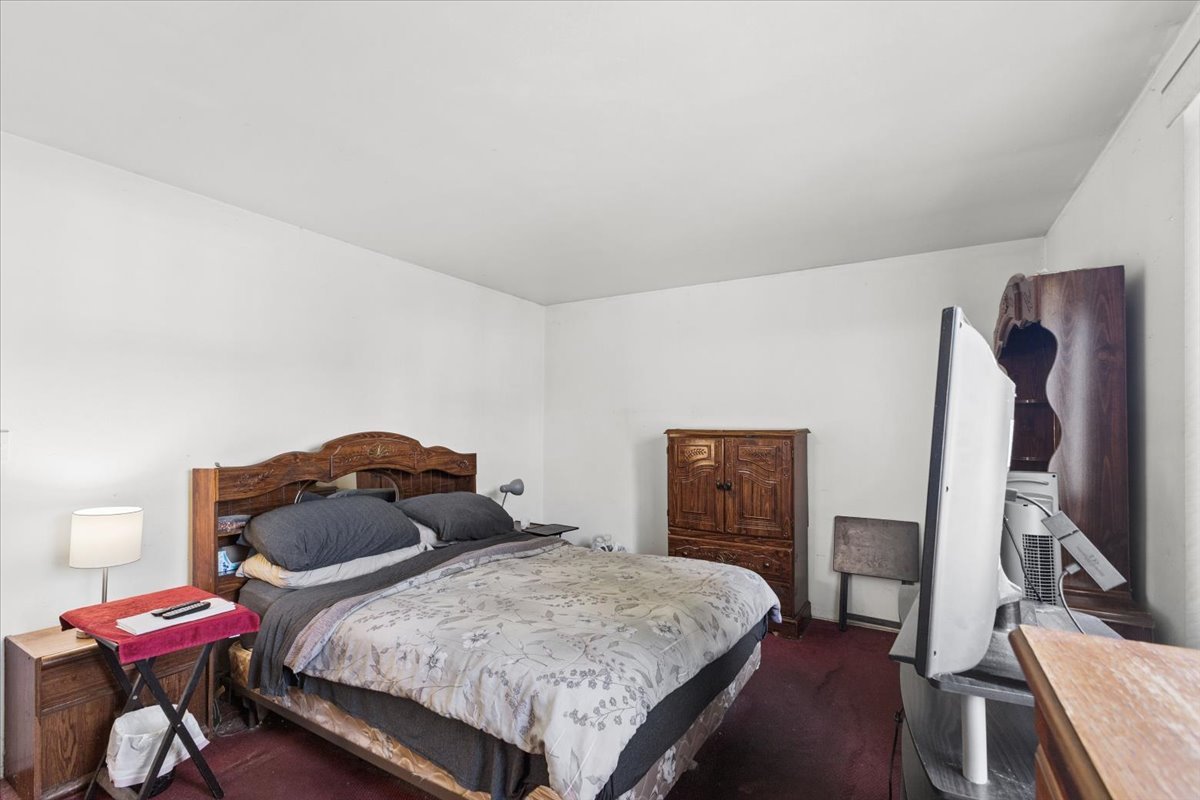 Bedroom with a large bed, carved wooden headboard, patterned duvet, and dark red carpet.