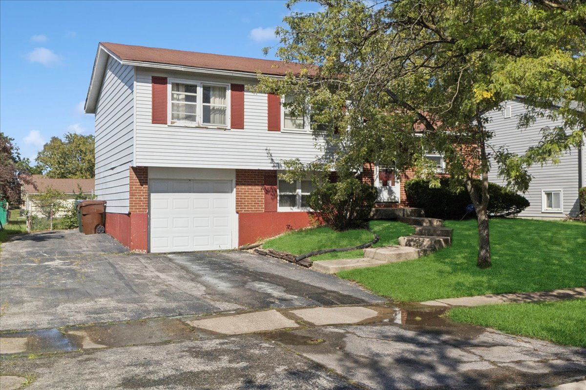 Split-level house with red shutters, an attached garage, and a tree-shaded front lawn.