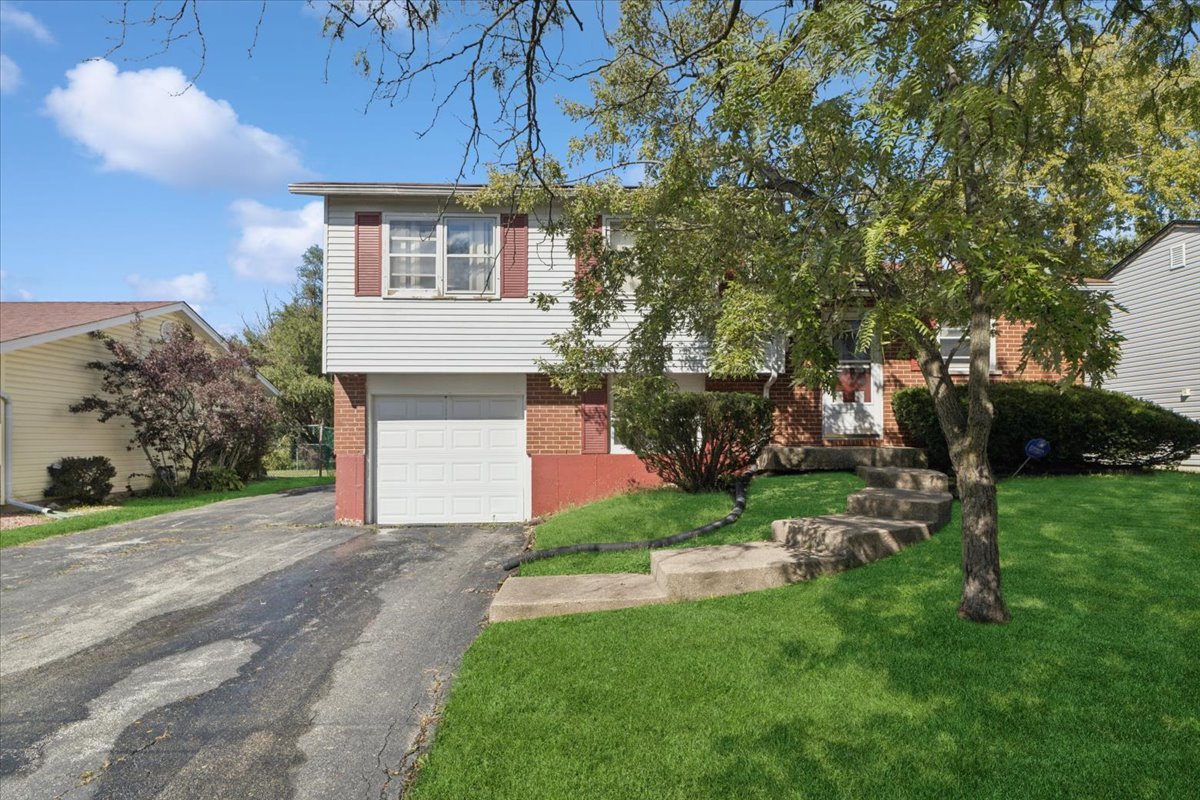 Split-level home with brick and siding, an attached garage, and front steps beneath a mature tree.