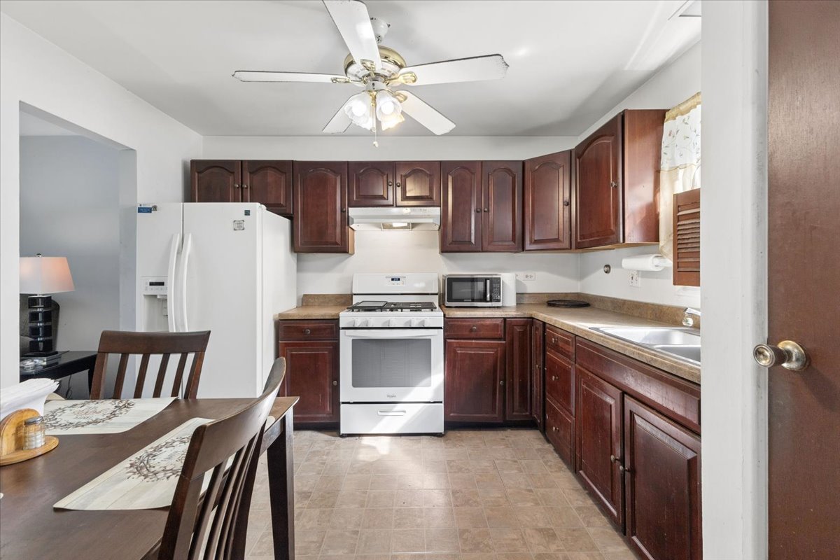 Kitchen with dark wood cabinets, tan countertops, and white appliances beside a dining table.