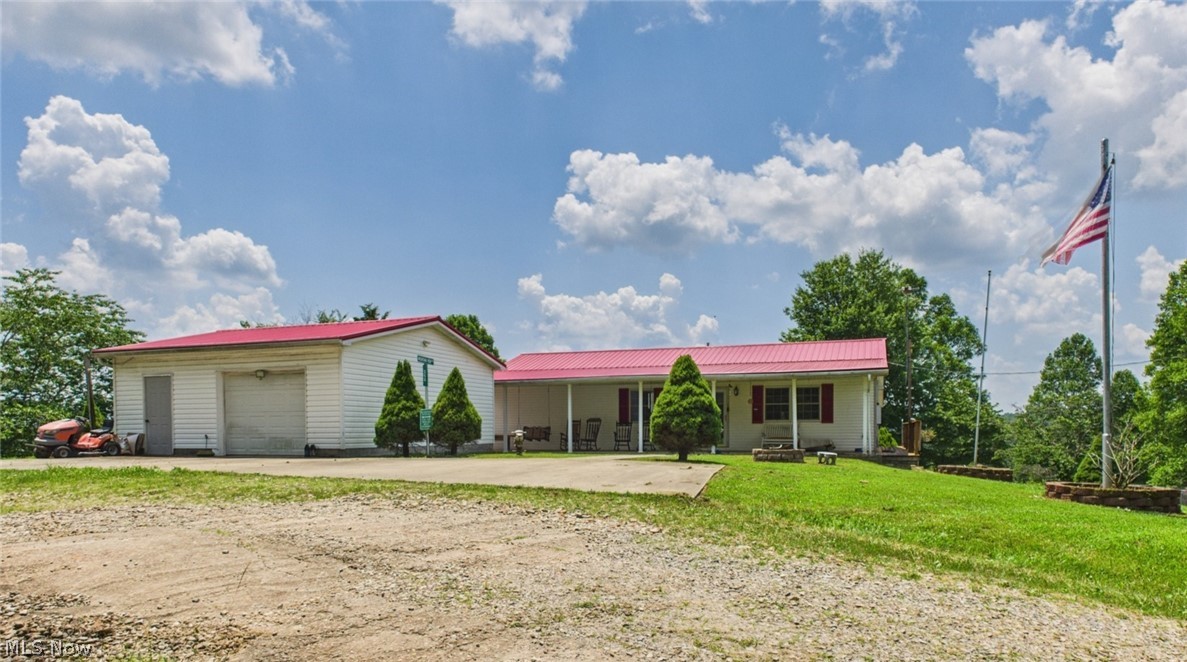 White ranch home with a red metal roof, detached garage, gravel driveway, and American flag.