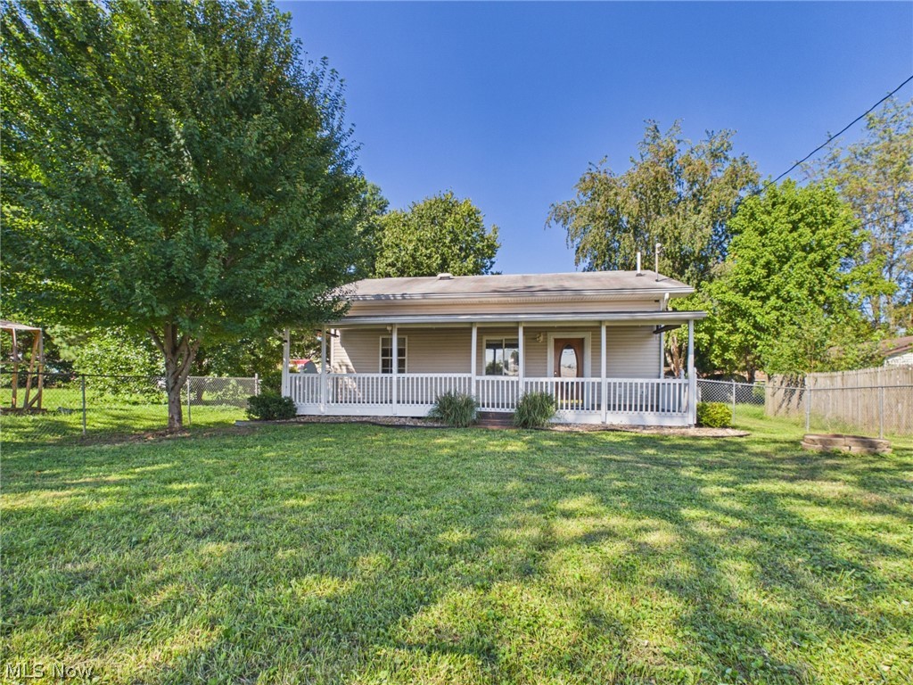 Single-story office with a long covered porch, broad lawn, mature trees, and a fenced yard.
