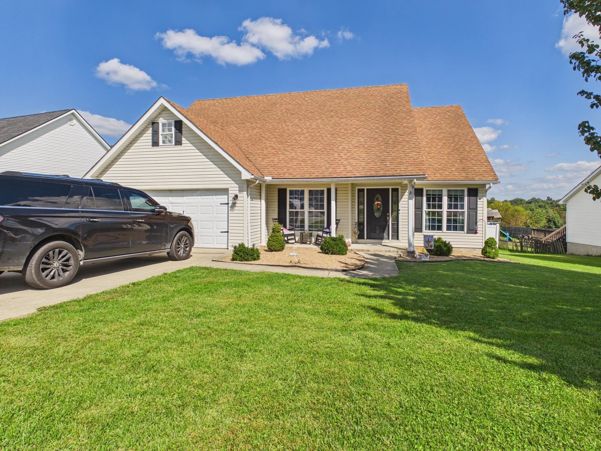 Cream-sided house with a broad tan roof, attached garage, covered porch, and black SUV in the driveway.