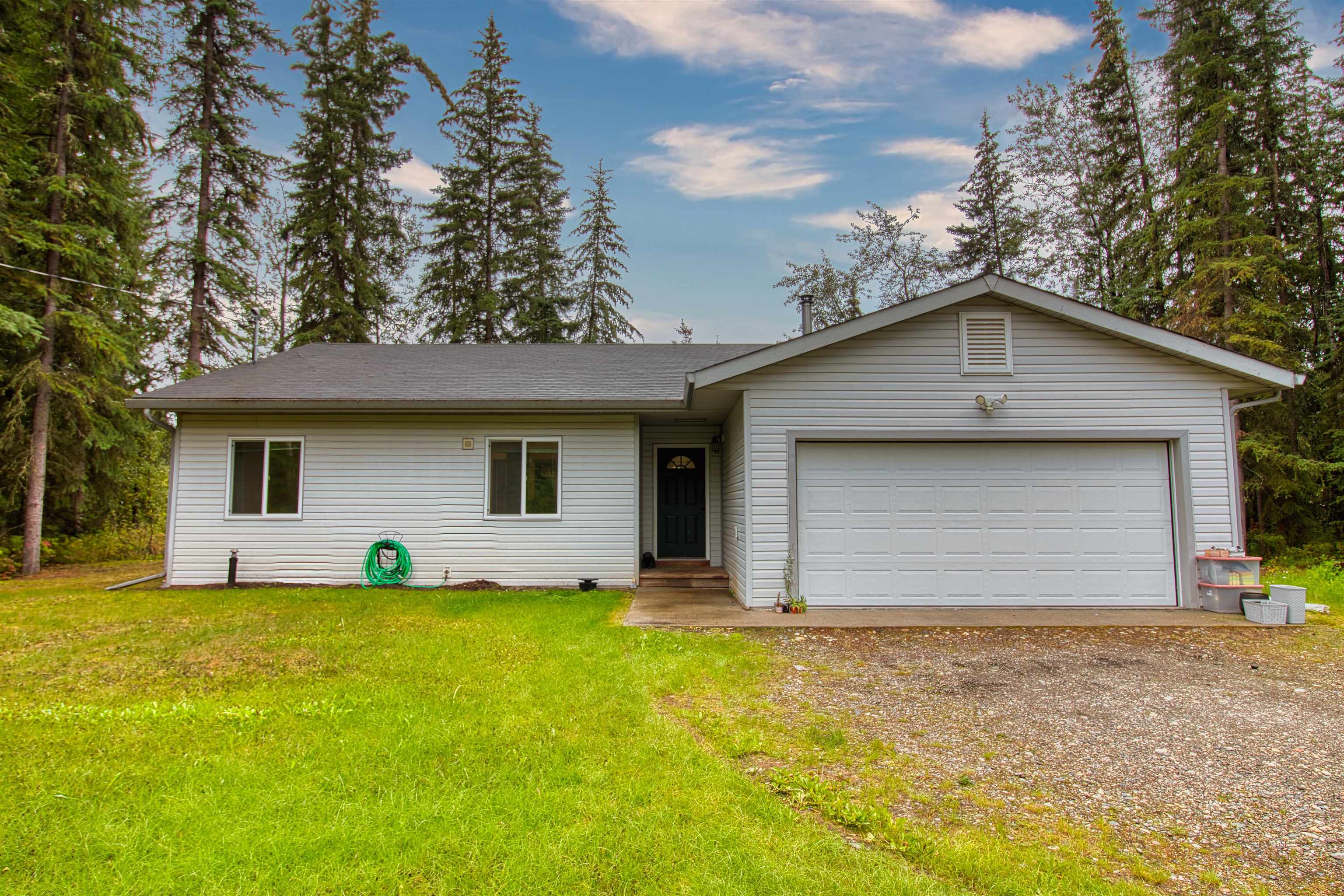Single-story gray home with an attached double garage, gravel driveway, and mature trees.