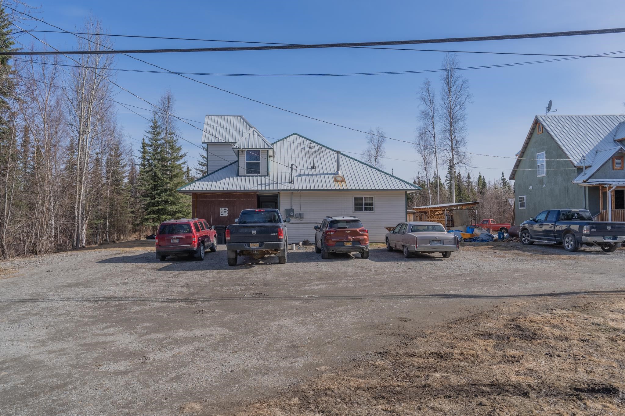 Light-colored home with a large metal roof and vehicles parked on a gravel driveway.
