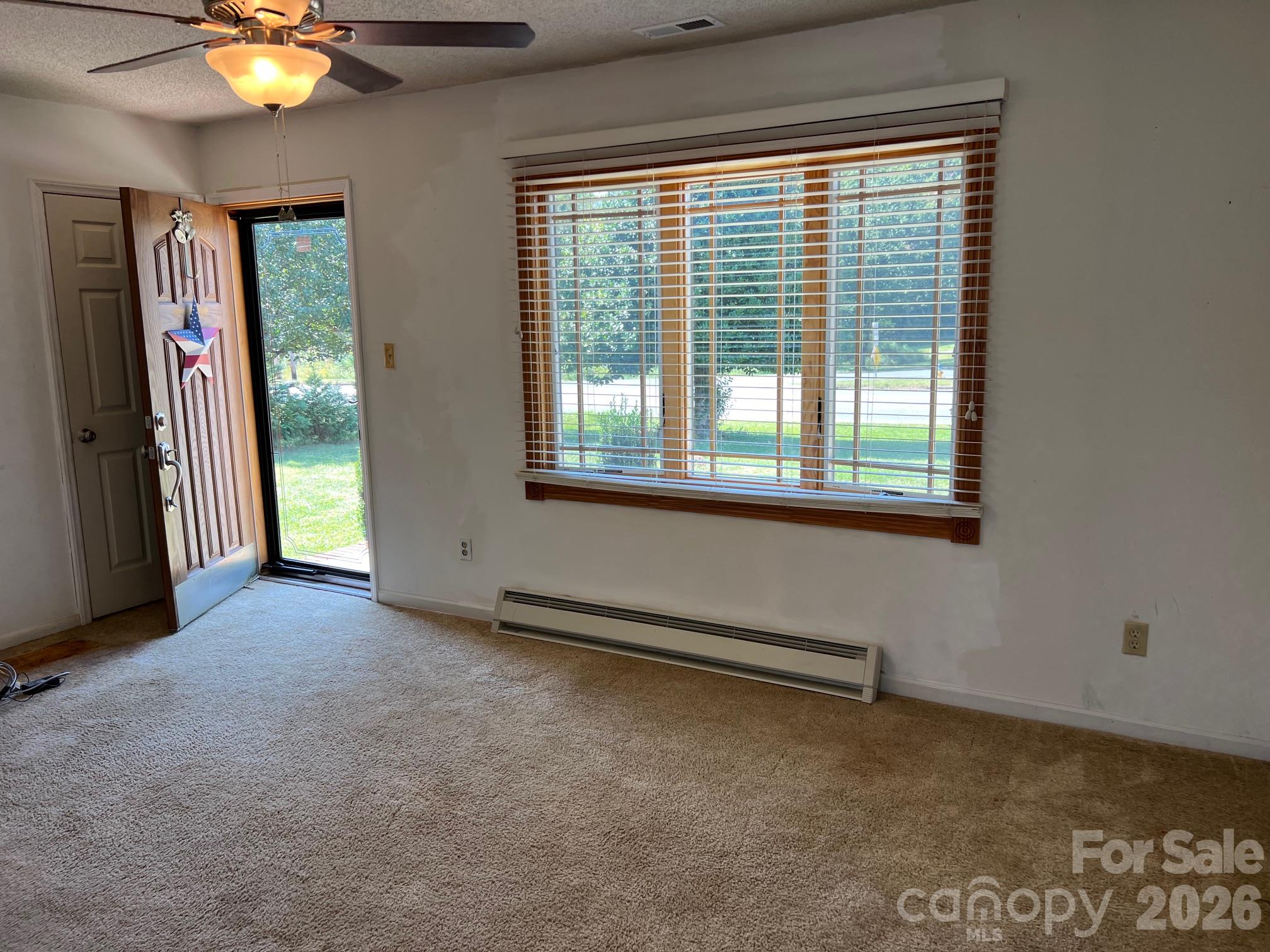 Vacant carpeted room with a ceiling fan, large window, and open front door.