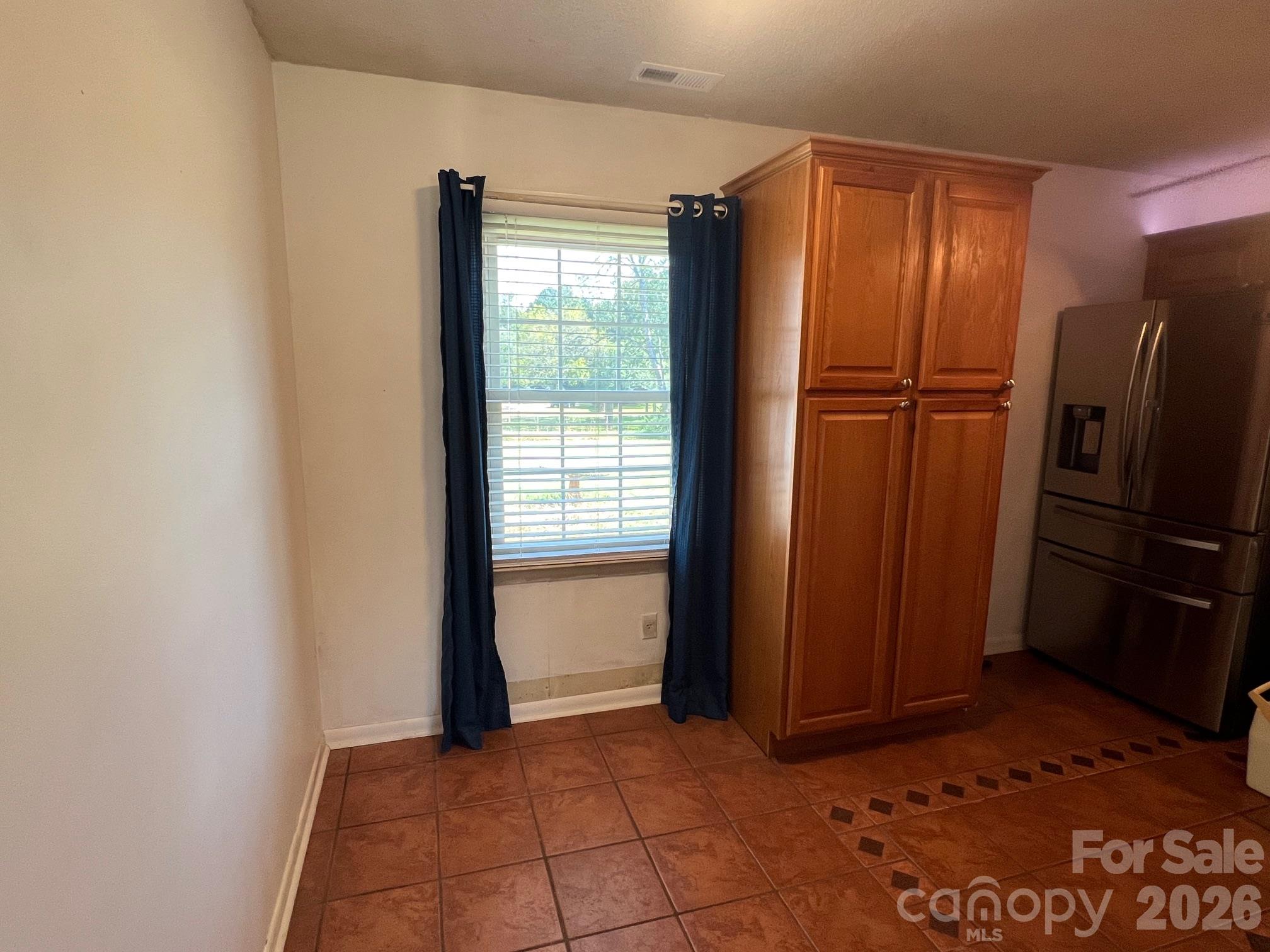Kitchen with tall wooden cabinets, a stainless steel refrigerator, and a curtained window.
