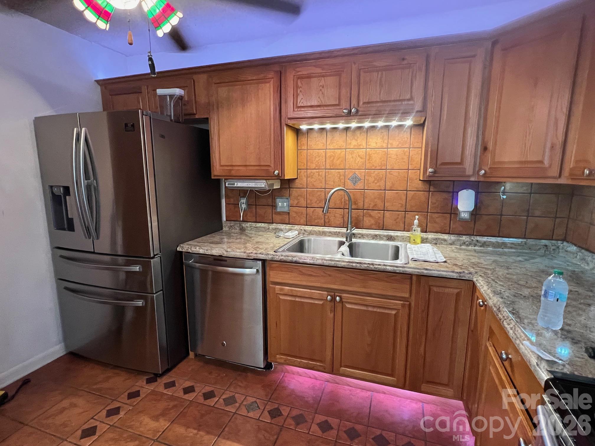 Kitchen with reddish wood cabinets, stainless steel appliances, tiled backsplash, and double-basin sink.