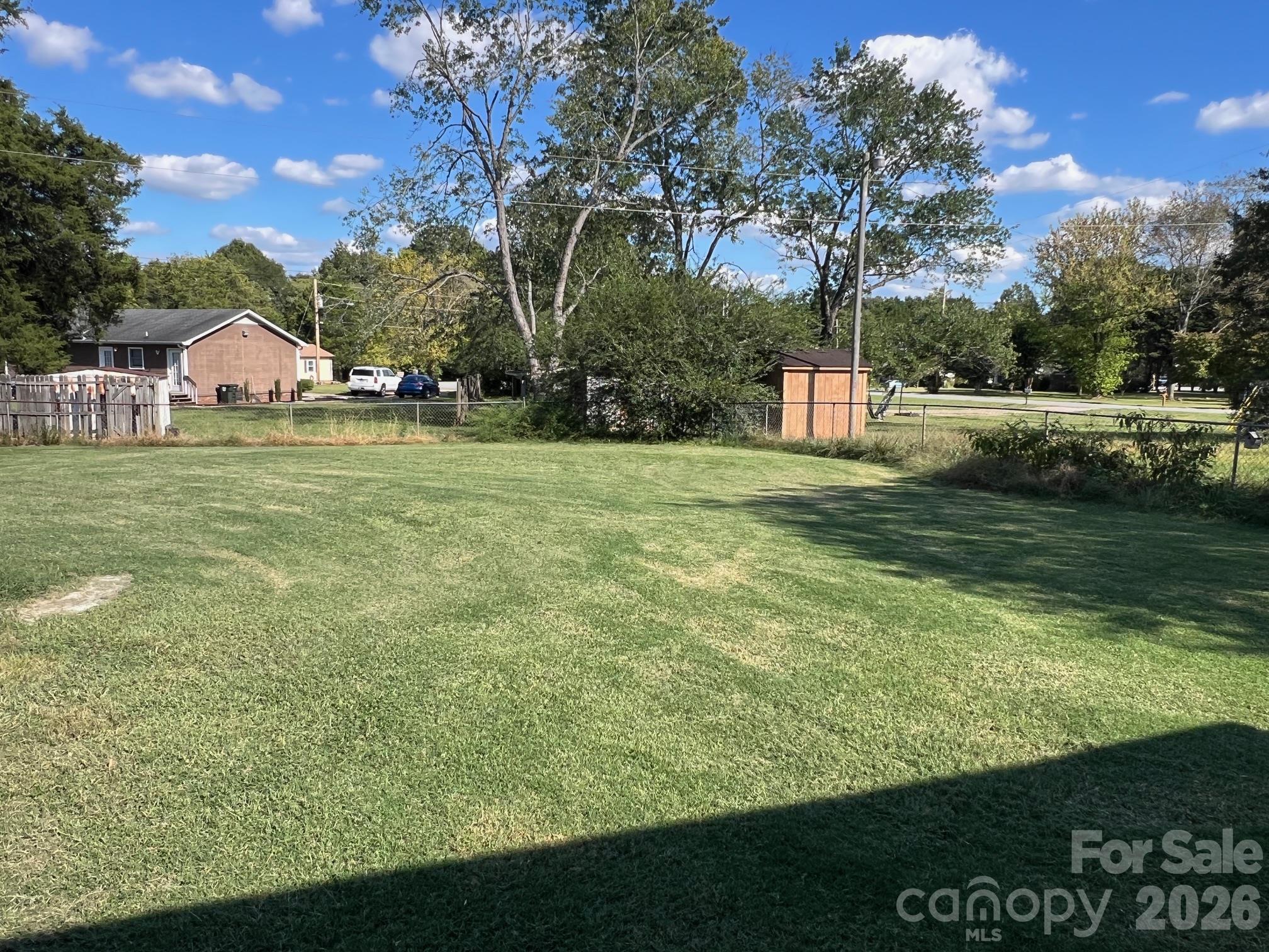 Grassy fenced property yard with a small wooden shed and mature trees.
