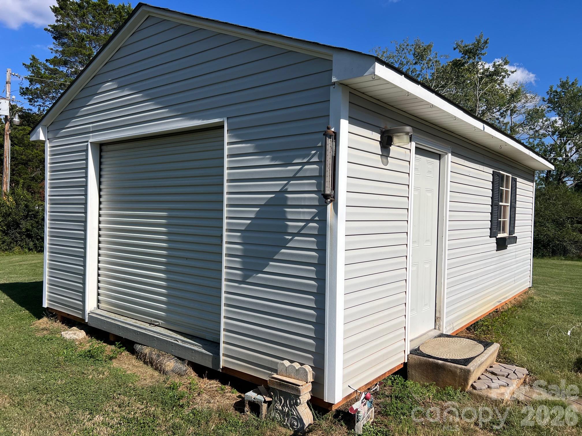 Detached white-sided outbuilding with a roll-up garage door and side entrance.