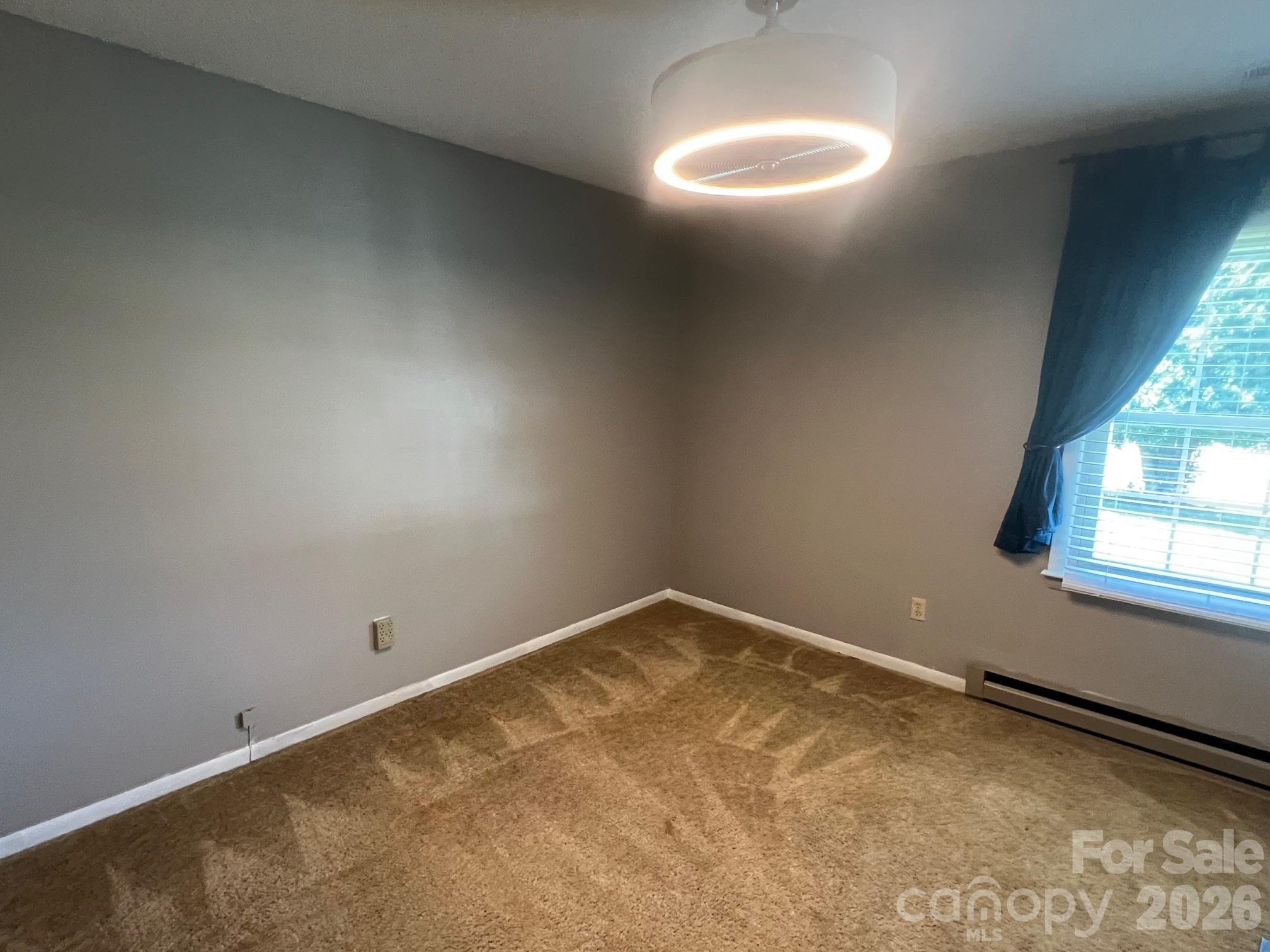 Empty carpeted room with gray walls, a round ceiling light, and a curtained window.