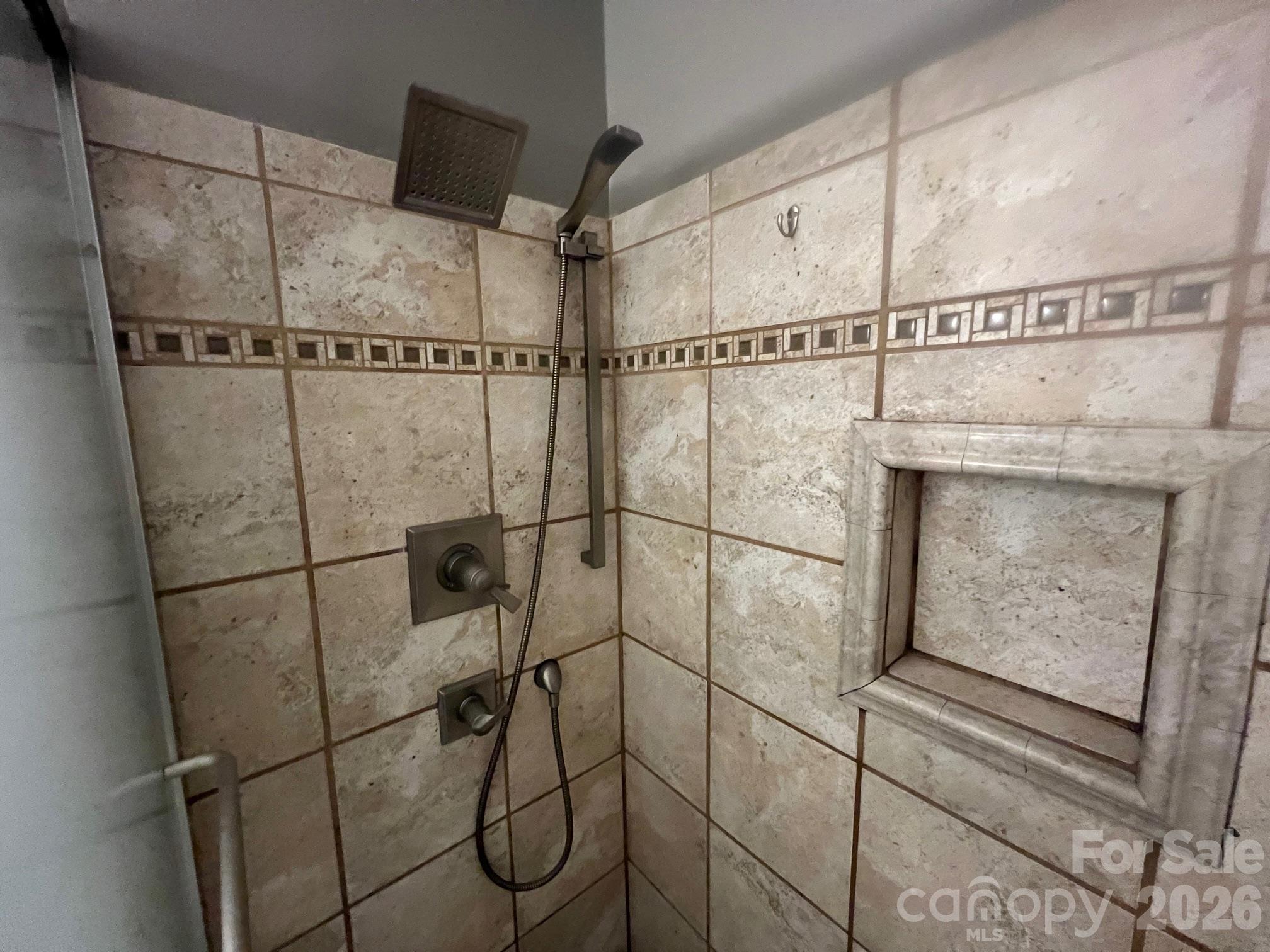 Tiled shower with a square rain showerhead, handheld wand, and recessed wall niche.
