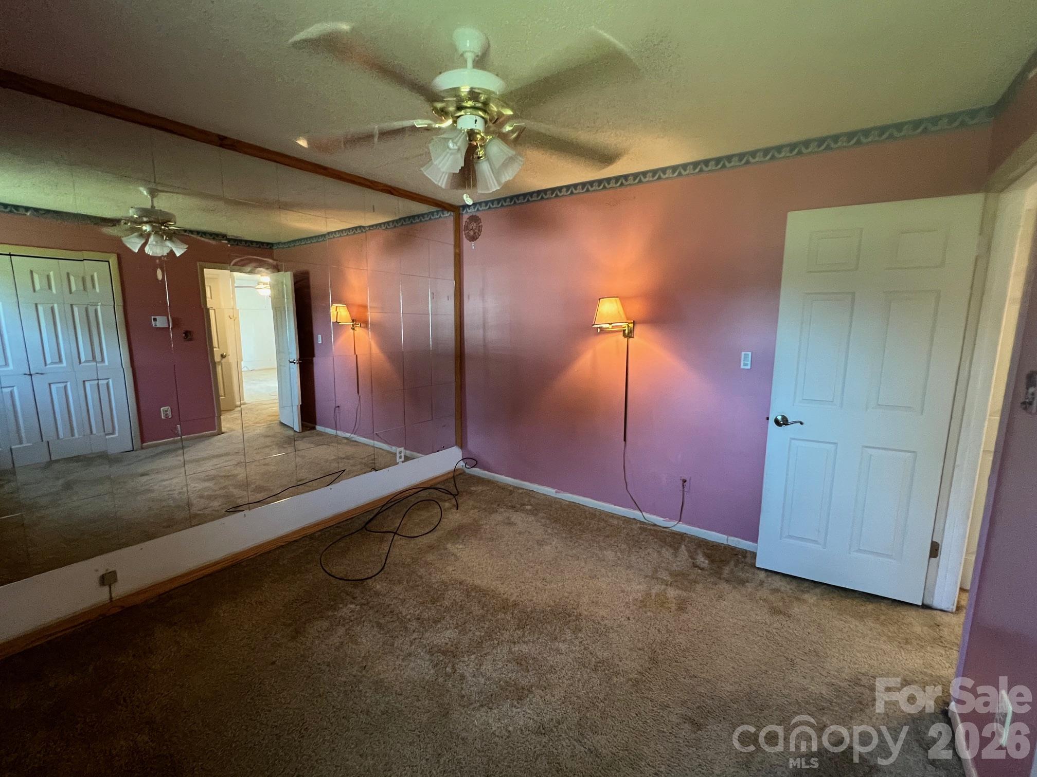 Empty bedroom with mauve walls, brown carpet, mirrored panels, and a ceiling fan.