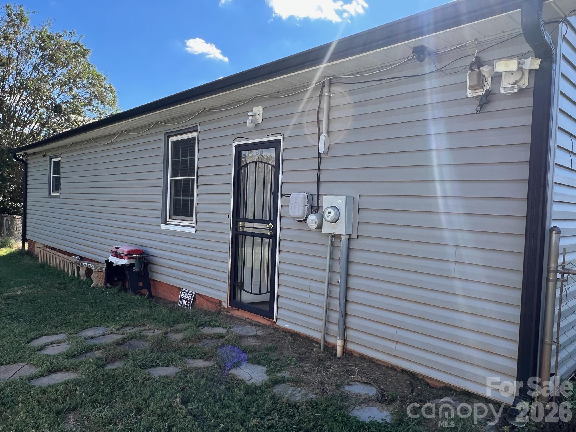 Home exterior with gray siding, a black security door, utility meters, and stepping stones in the grass.