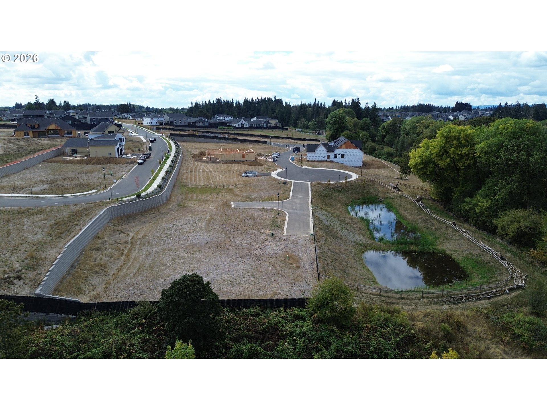 Aerial view of a developing neighborhood with cleared lots, winding streets, and a fenced pond.