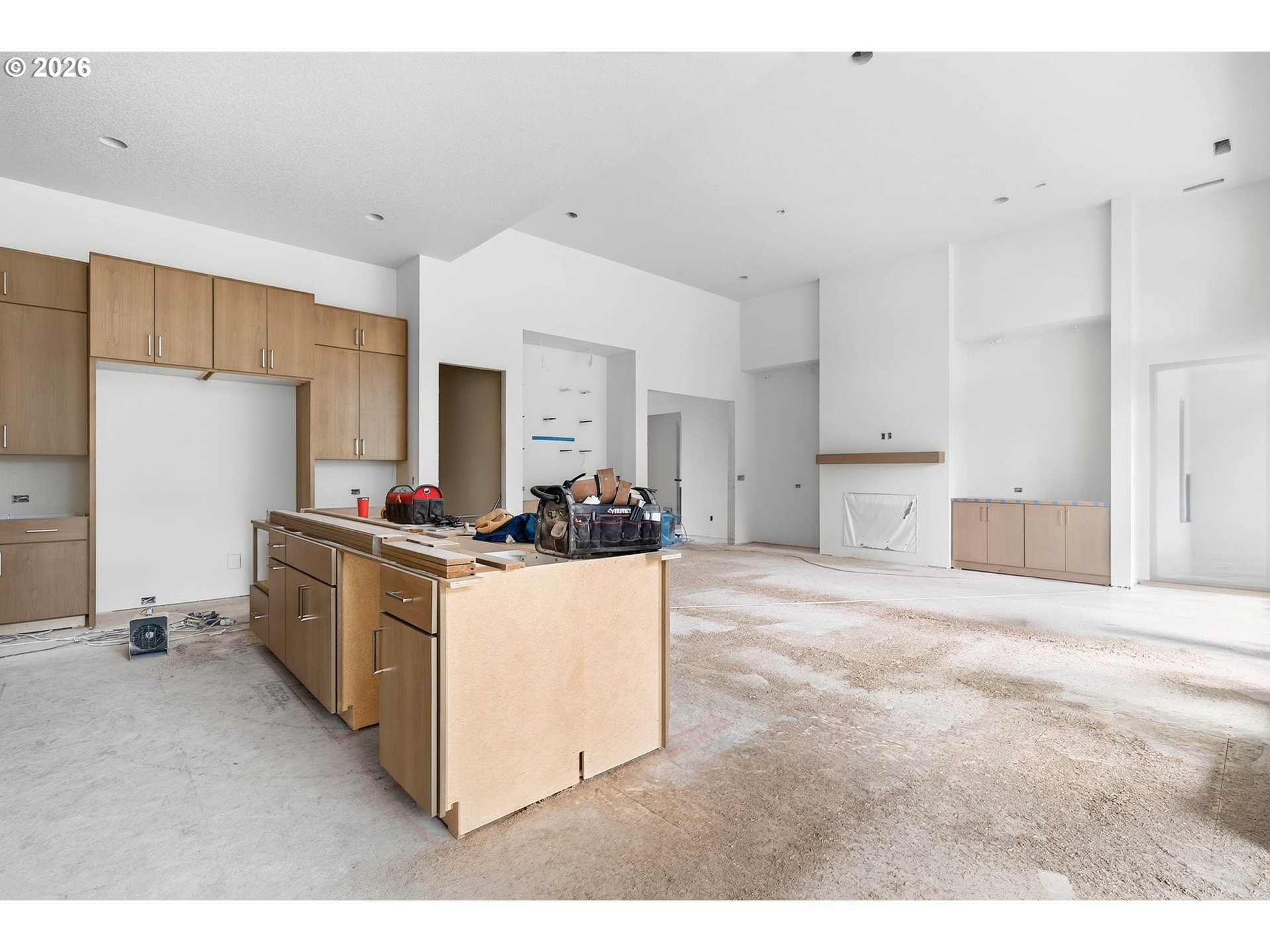 Unfinished kitchen with light wood cabinetry, a large island, and a bare construction floor.