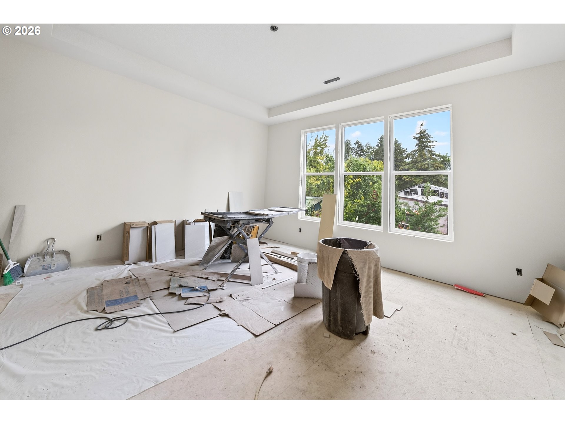 Unfinished room under renovation, with floor coverings and tools beside three large windows.