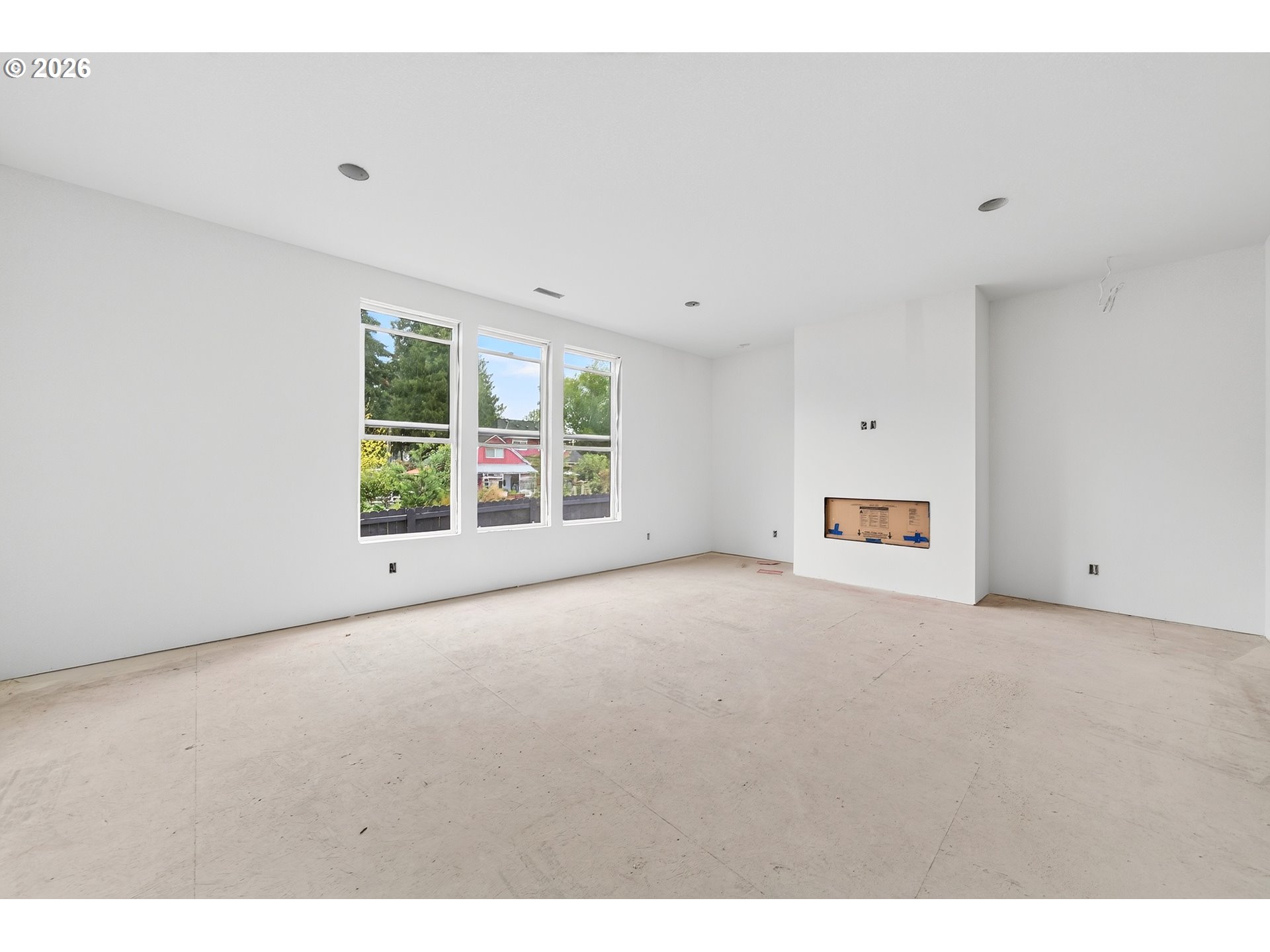 Unfinished living room with three tall windows and a recessed fireplace opening.