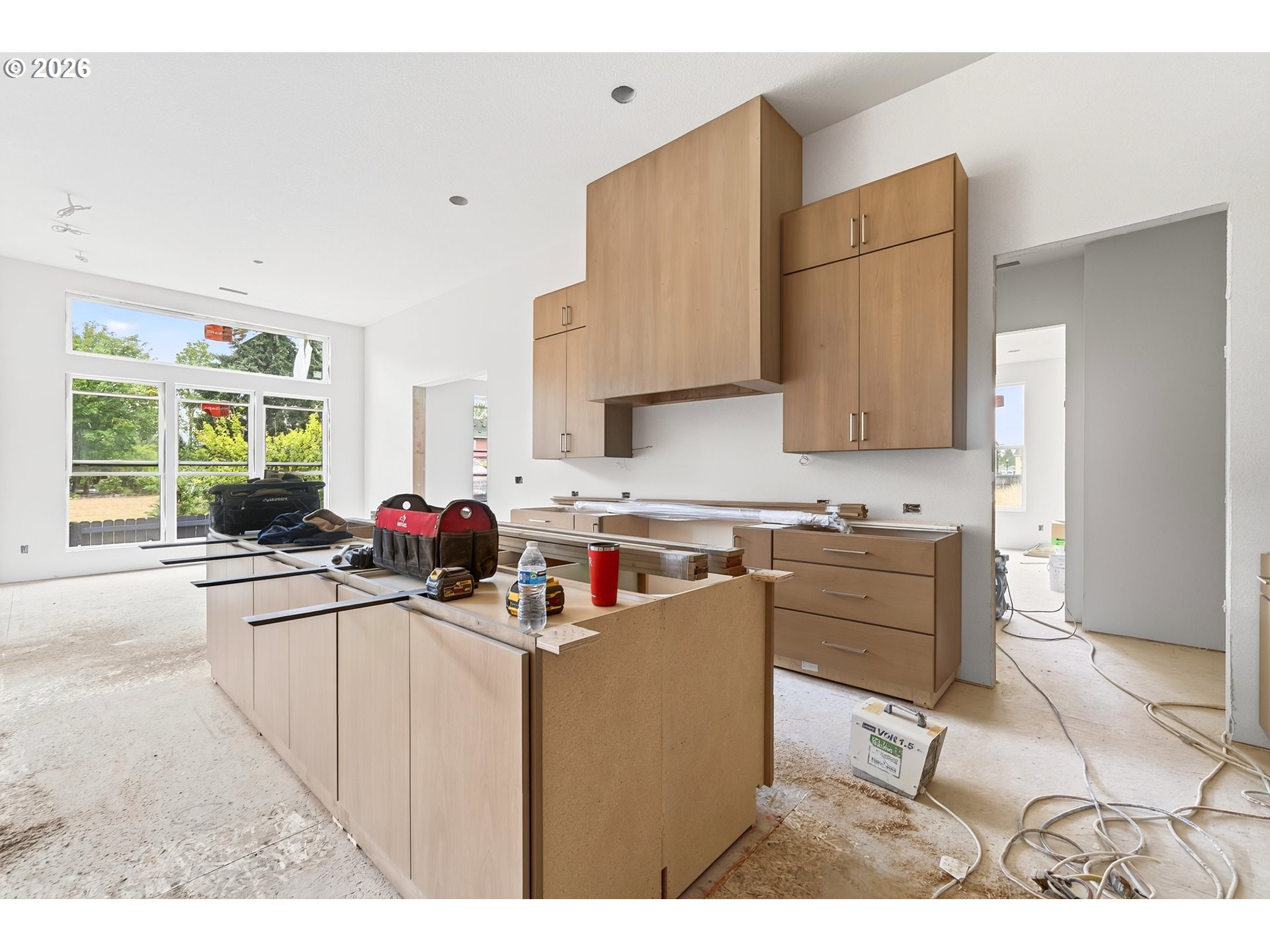 Kitchen under construction with light wood cabinets, a large island, and tools scattered across the counters.