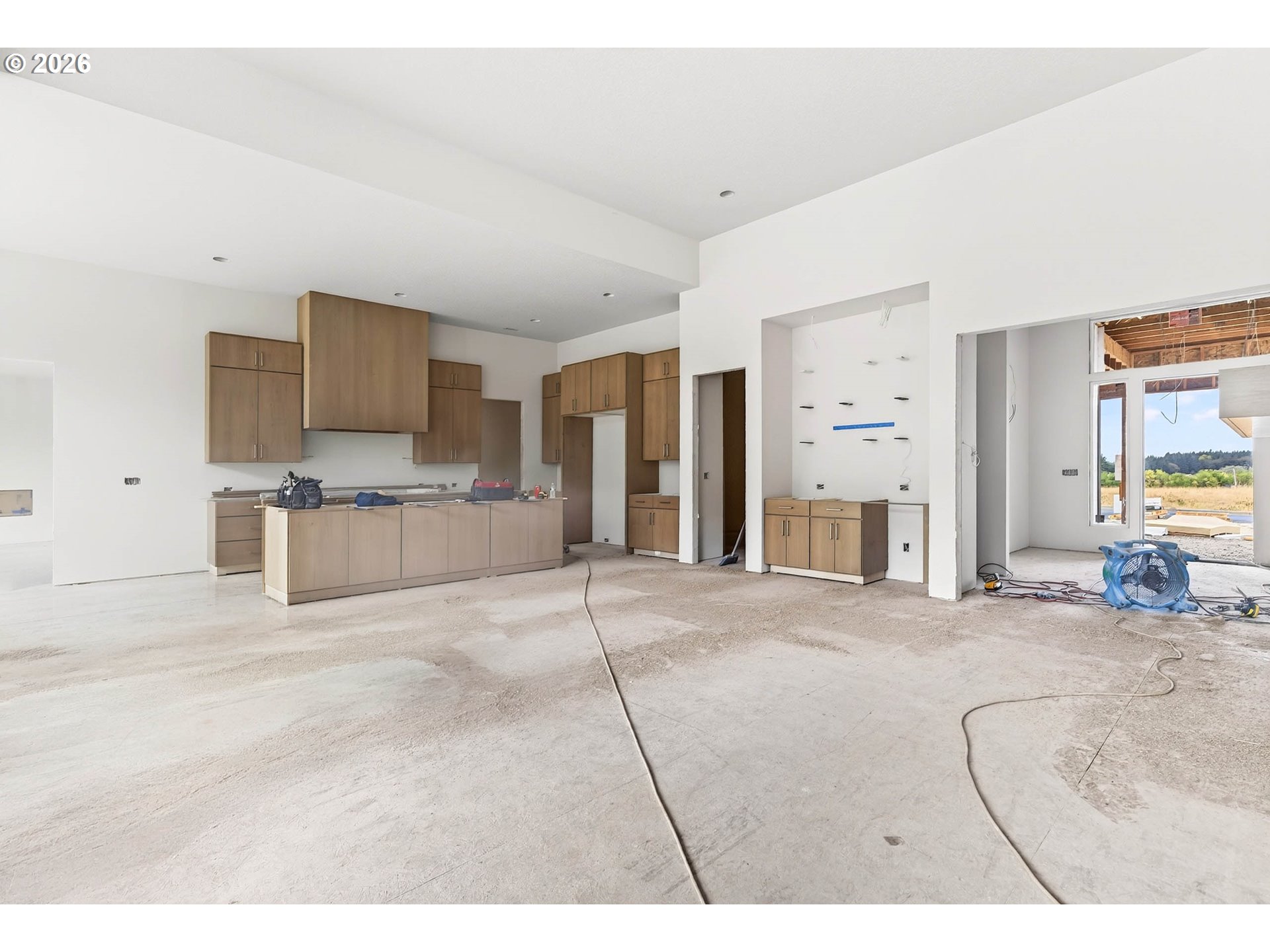 Kitchen under construction with light wood cabinets, a large island, and unfinished concrete flooring.