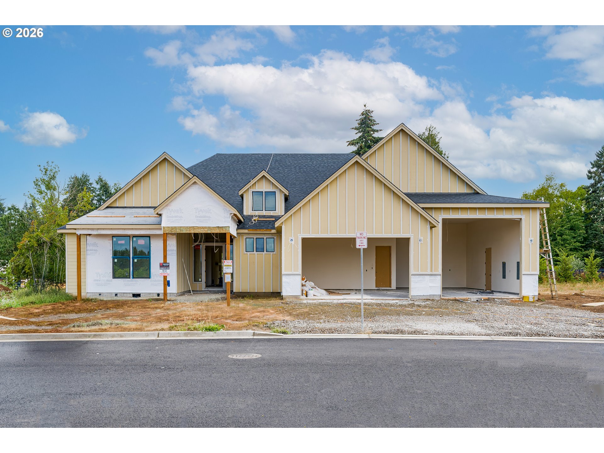 House under construction with tan siding, multiple gables, and two open garage bays.