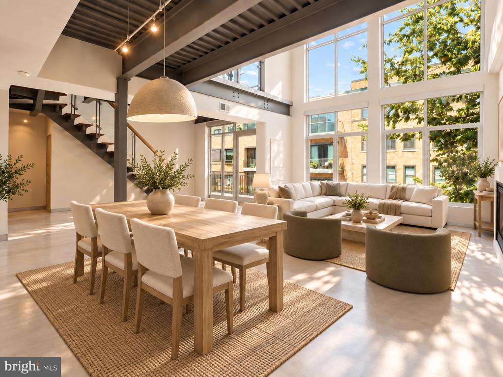 Open-plan dining and living room with exposed beams, a wooden table, and tall sunlit windows.