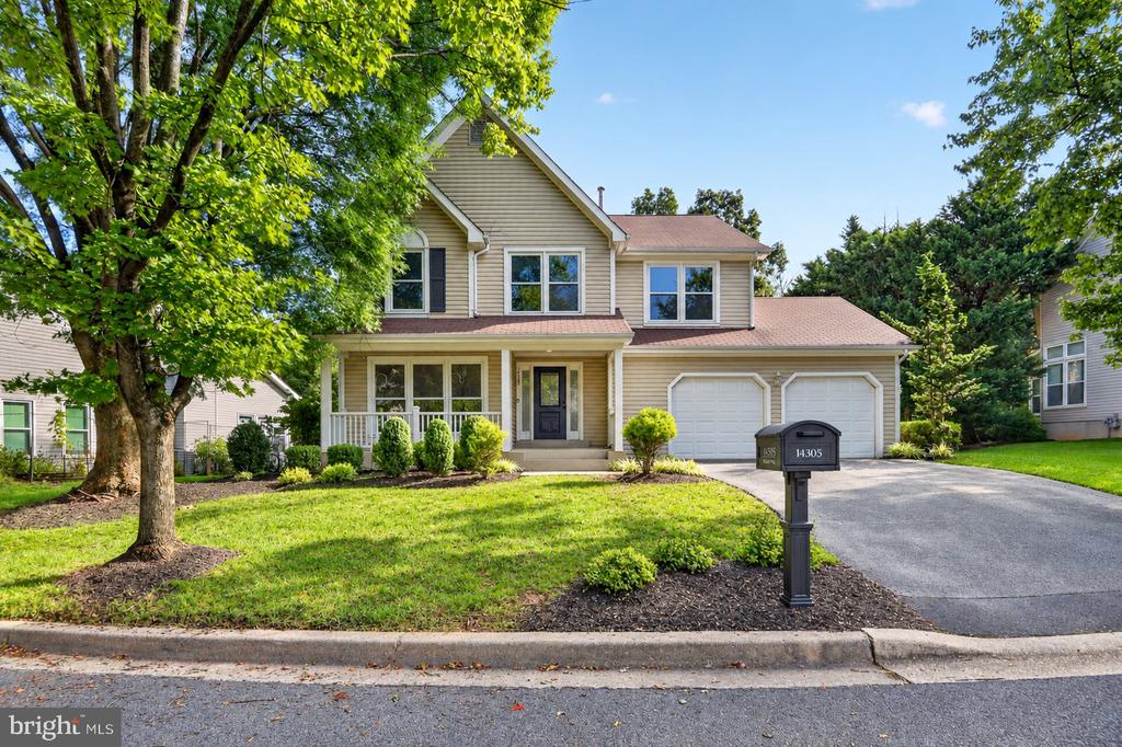 Two-story beige house with a covered porch, double garage, and landscaped front lawn.