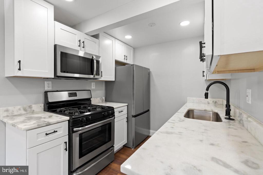 Kitchen with white cabinetry, marble-look counters, stainless-steel appliances, and a black faucet.