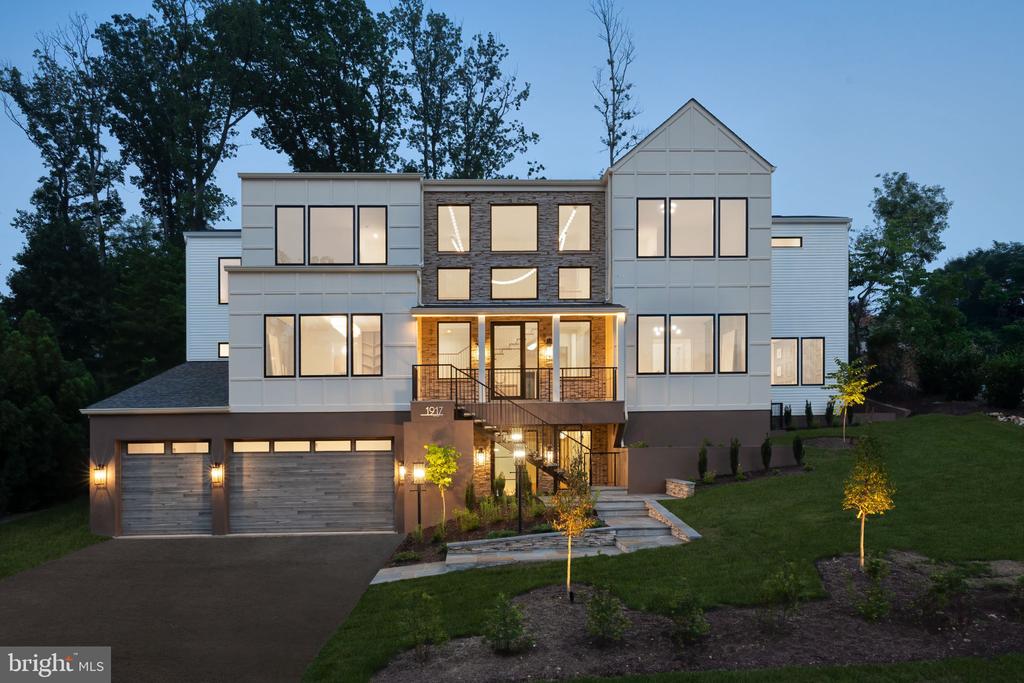 Modern multi-story home with illuminated windows, a covered balcony, and an attached two-car garage at dusk.