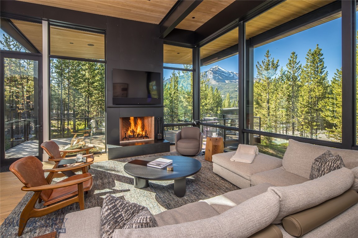 Furnished living room with a fireplace and floor-to-ceiling windows overlooking a mountain.