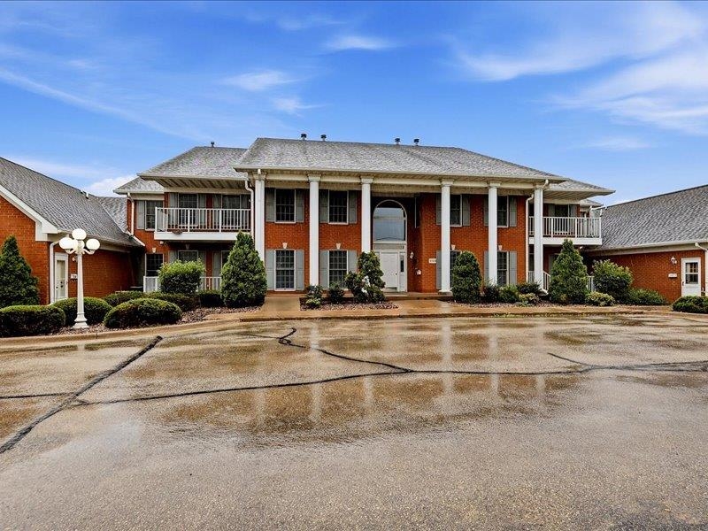 Red-brick multi-unit building with a columned entrance, side balconies, and wet pavement in front.