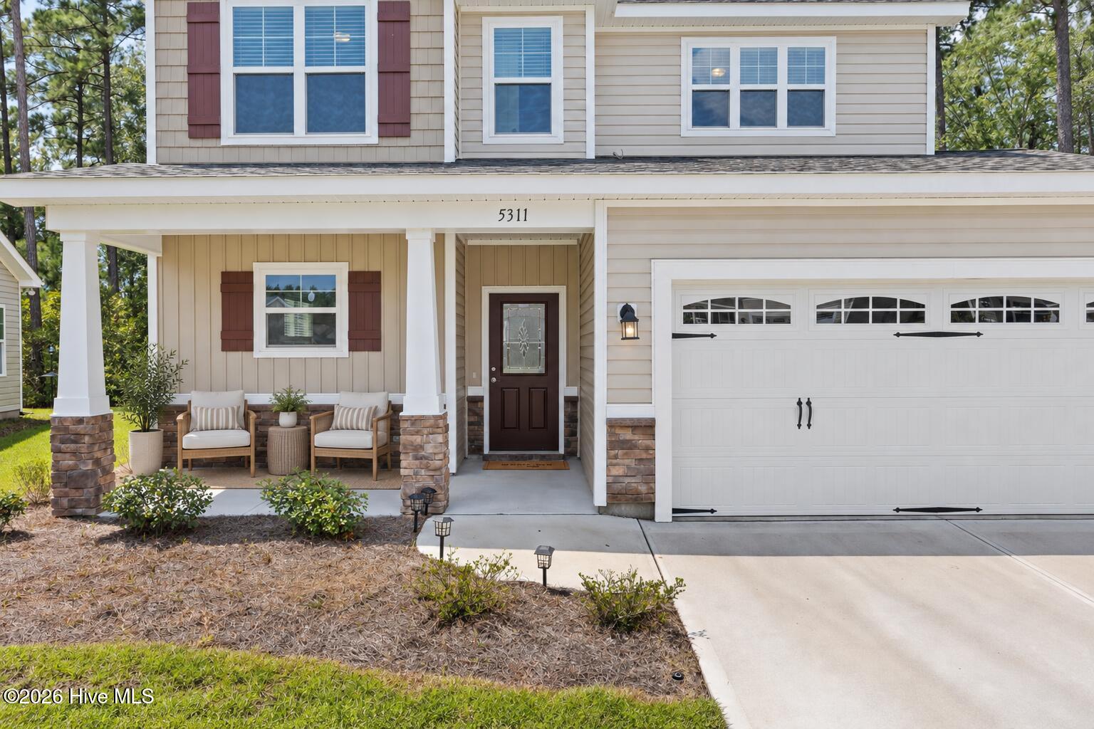 Two-story home with a furnished covered porch, red shutters, and an attached double garage.