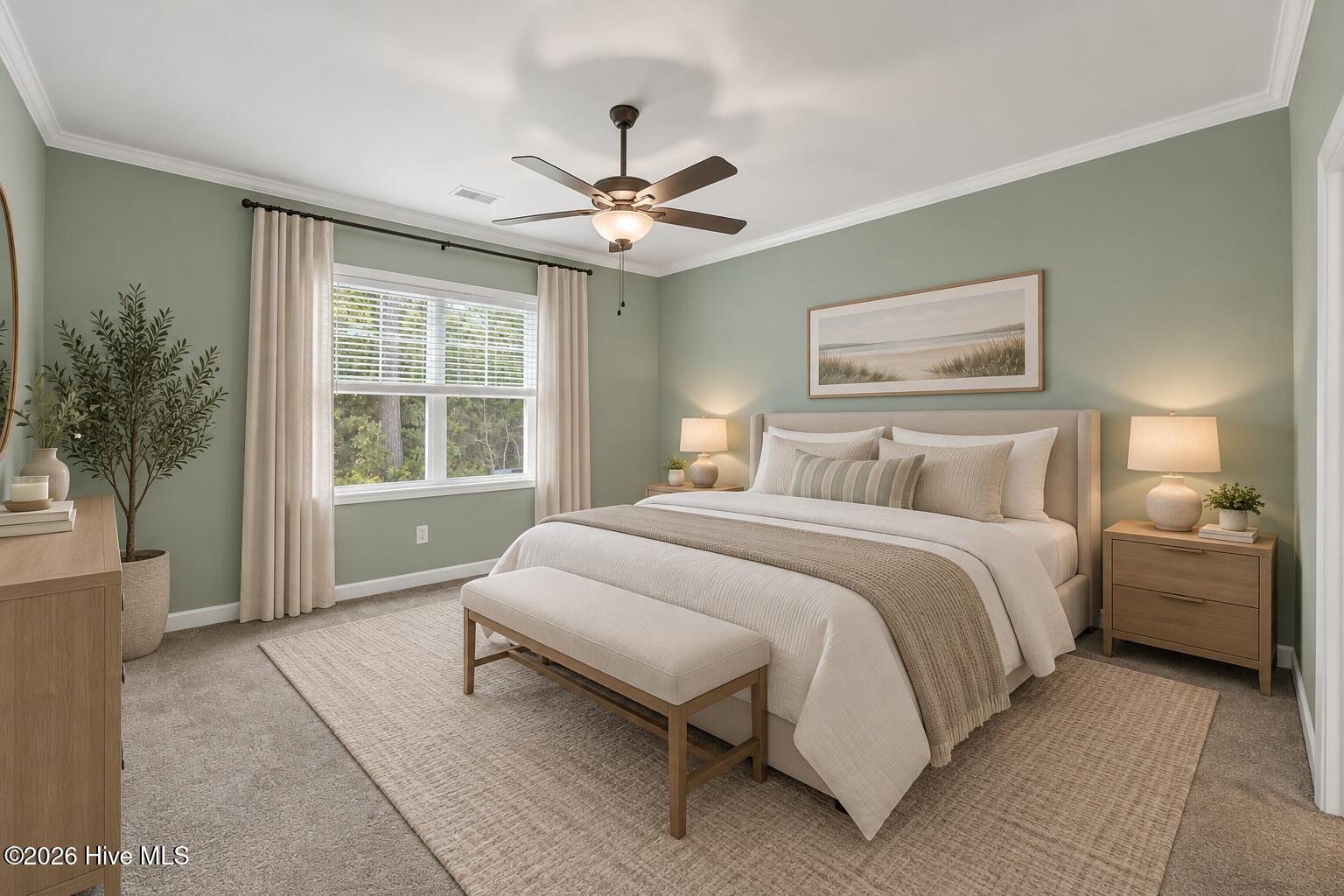 Staged bedroom with sage-green walls, neutral bedding, a foot-of-bed bench, and a window overlooking trees.