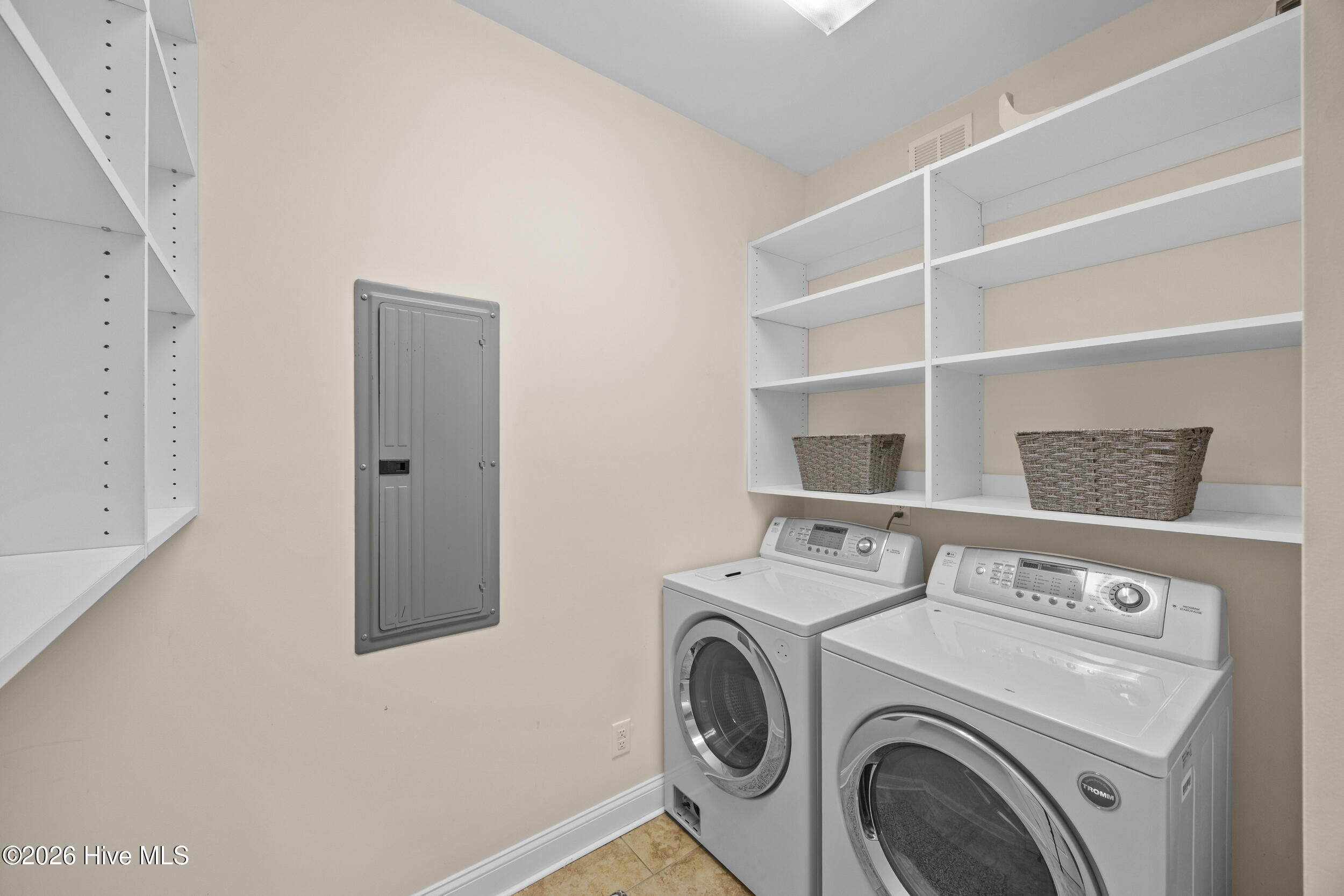 Laundry room with front-loading washer and dryer beneath white shelving with woven baskets.