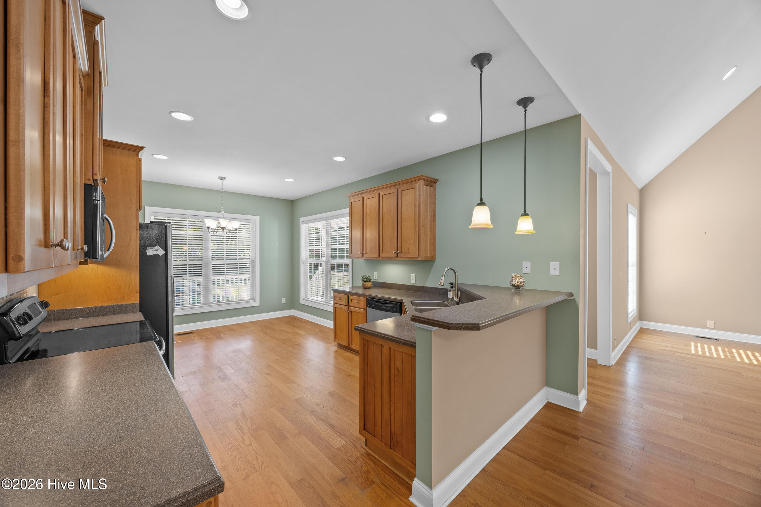 Kitchen with wood cabinets, dark countertops, a sink peninsula, sage-green walls, and hardwood floors.