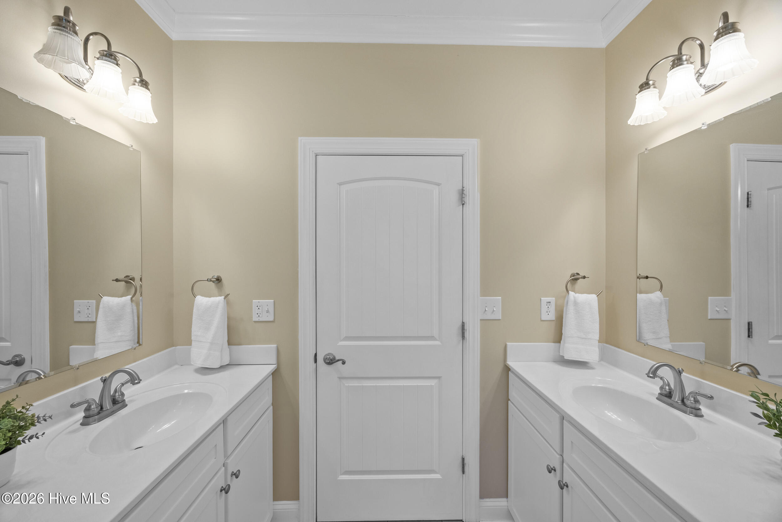 Bathroom with a white double-sink vanity, large mirrors, and a paneled door between the sinks.