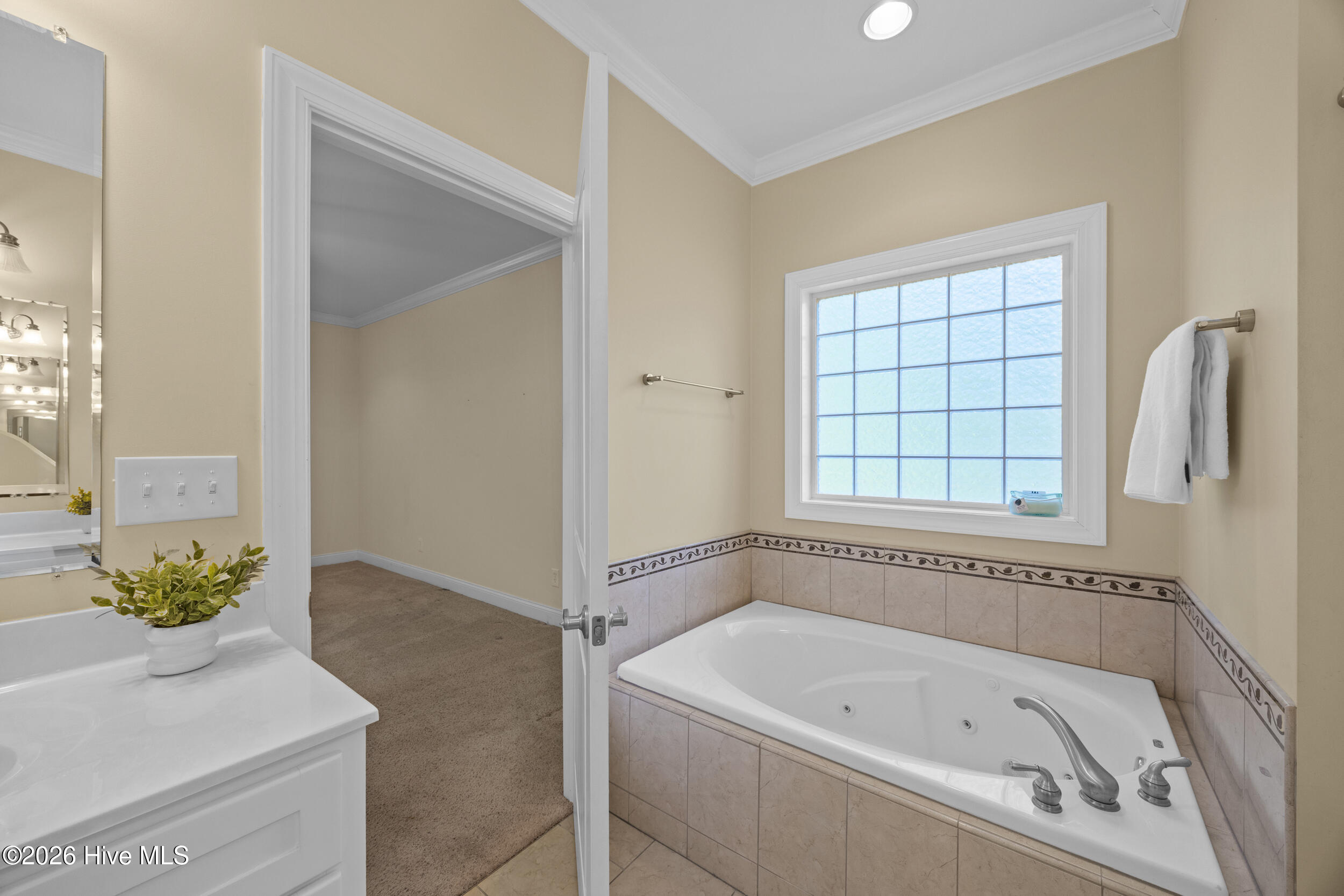 Bathroom with a jetted tub beneath a gridded window and a white vanity.