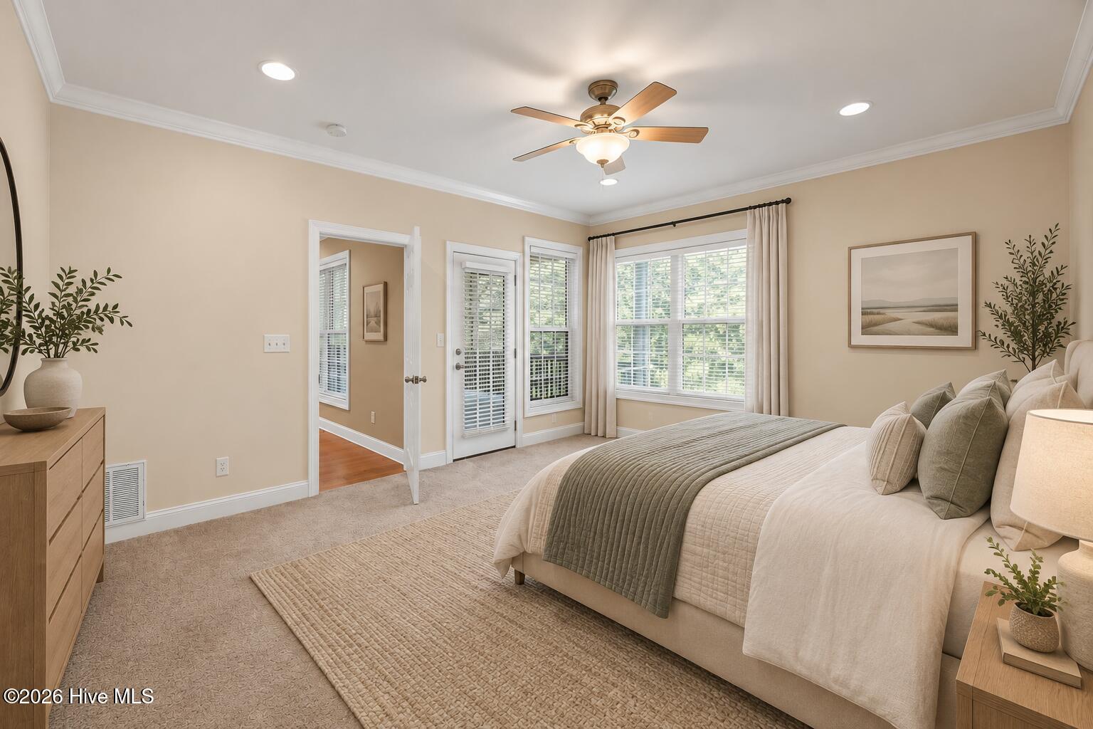 Bright staged bedroom with a large bed, ceiling fan, and windows with plantation shutters.