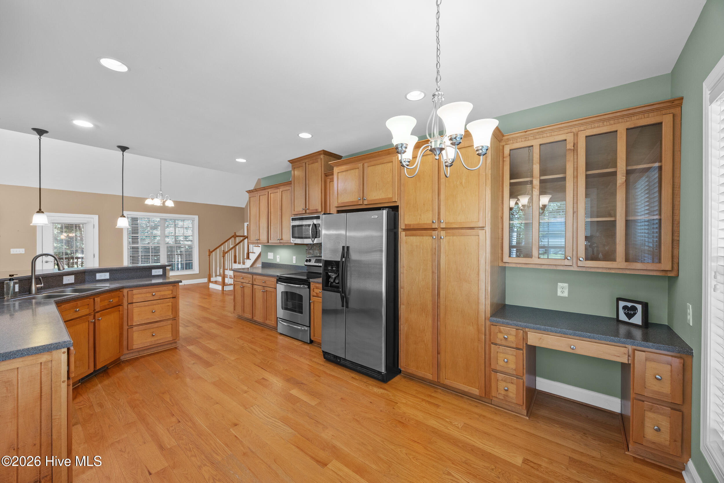 Kitchen with wood cabinetry, stainless steel appliances, hardwood floors, and a built-in desk.
