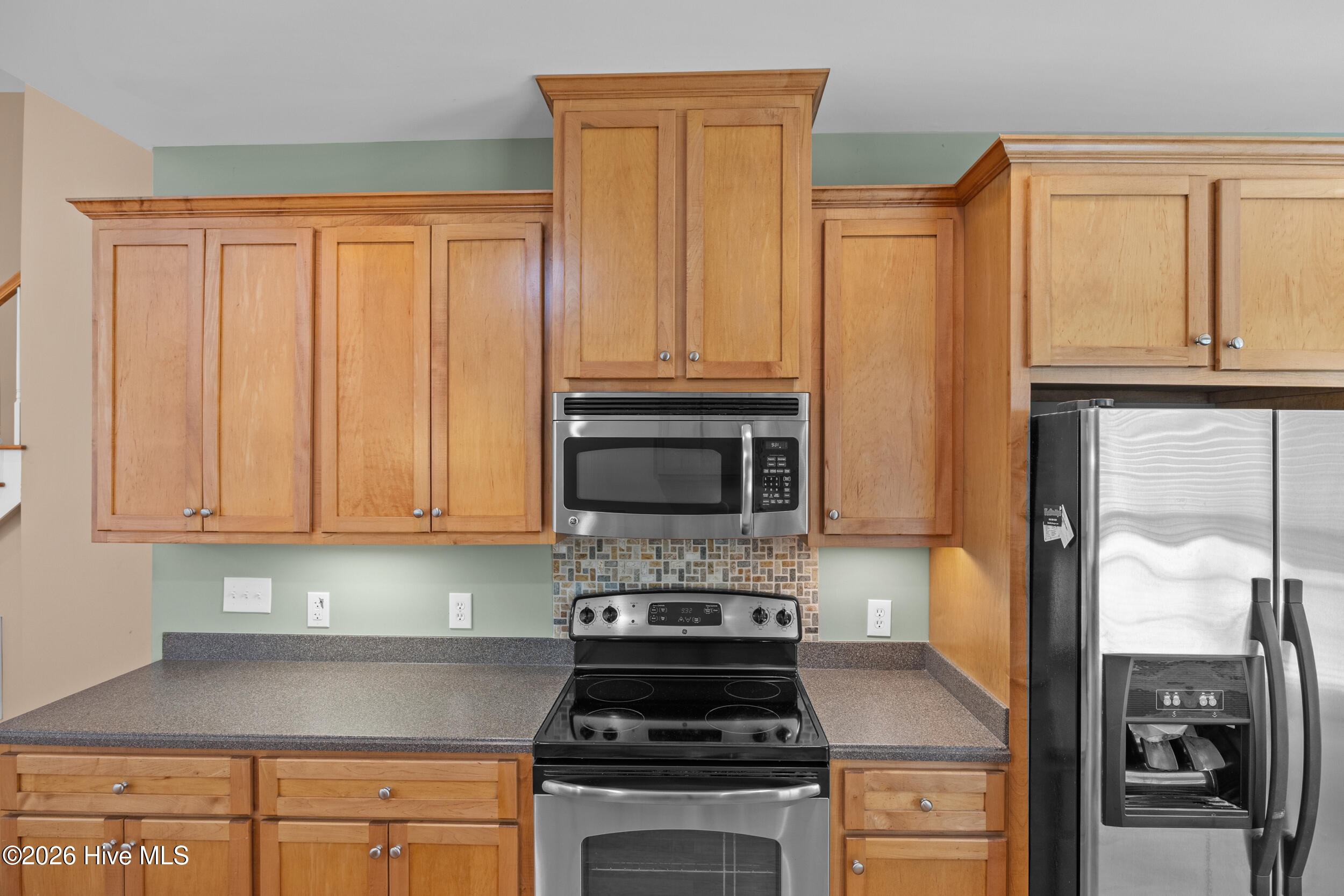 Kitchen with wood cabinets, gray countertops, stainless steel appliances, and a patterned tile backsplash.